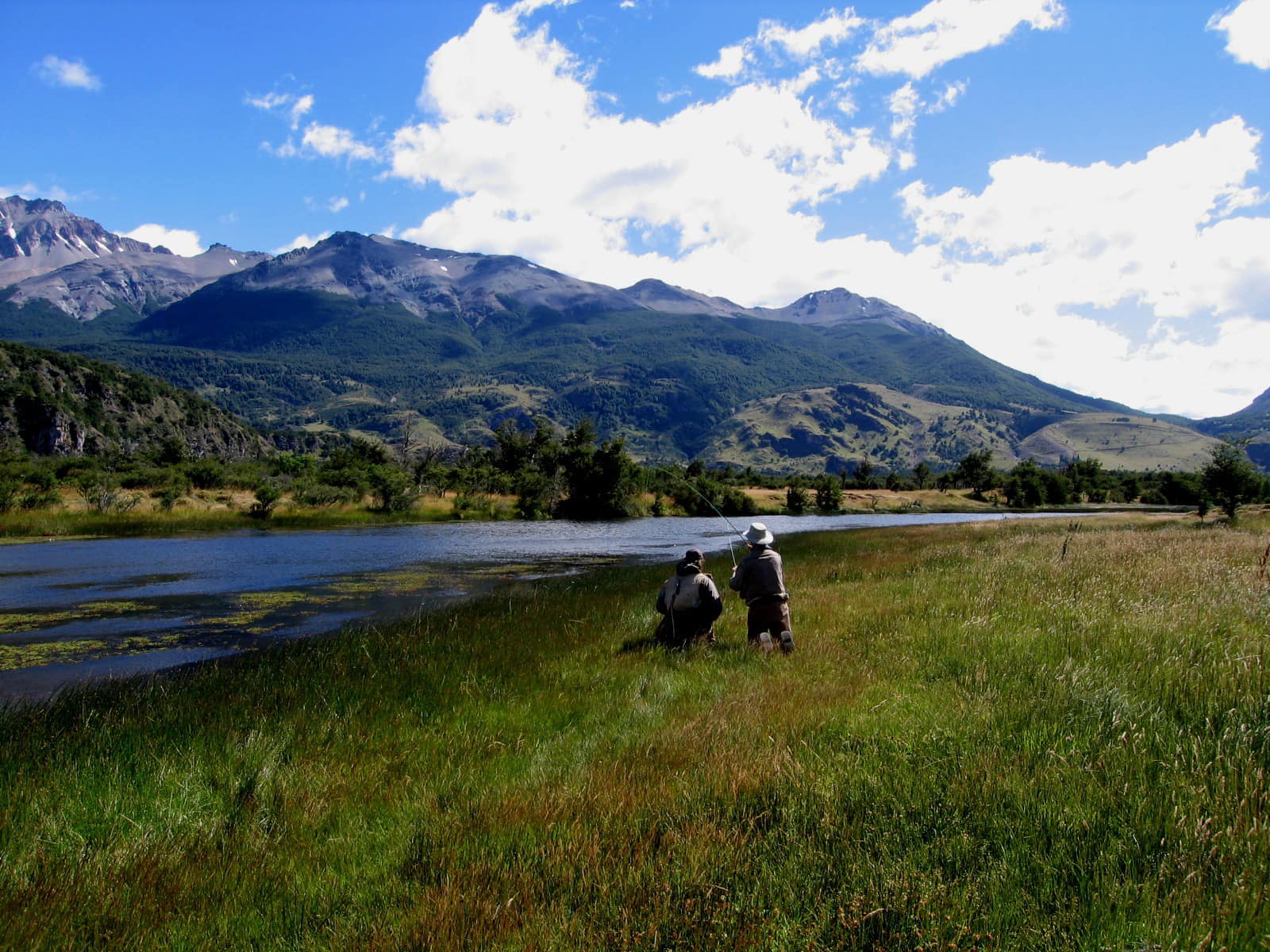 Anglers fishing a grassy bend of the Ñirehuao River at El Saltamontes Lodge