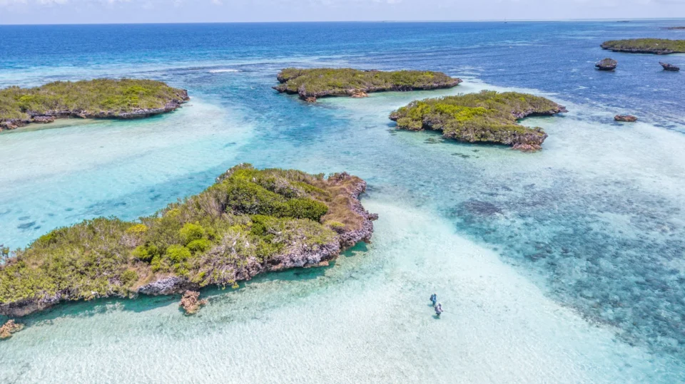 Aerial of Cosmoledo cays and wading anglers on turquoise flats, Seychelles