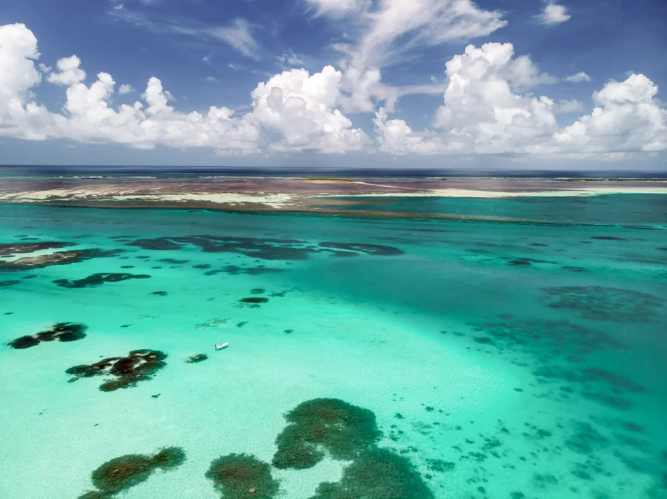 Aerial of Cosmoledo turquoise flats and a lone skiff, Seychelles