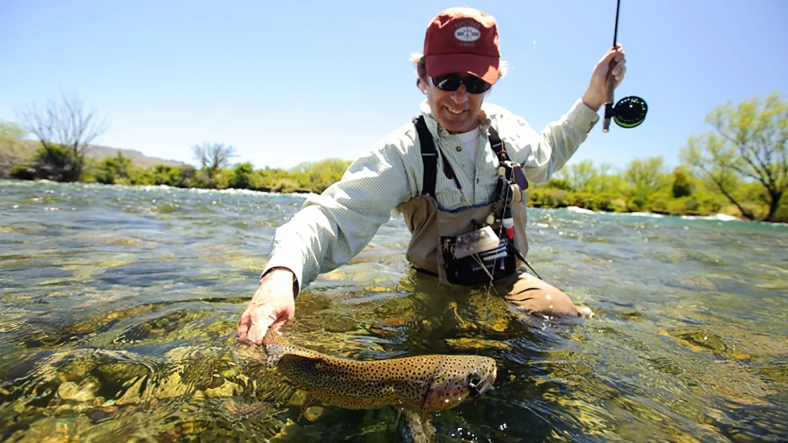 Angler in waders holding a brown trout in clear Chimehuín water at Tipiliuke Lodge, Patagonia, Argentina