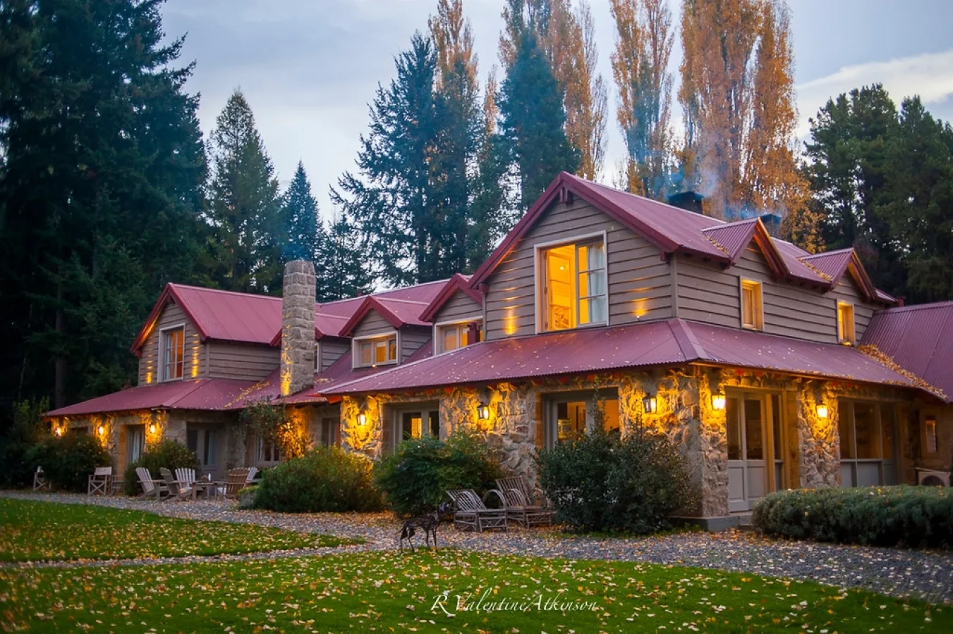 Tipiliuke Lodge at dusk in autumn, stone and wood lodge with red roof, lanterns, and Adirondack chairs, Patagonia, Argentina