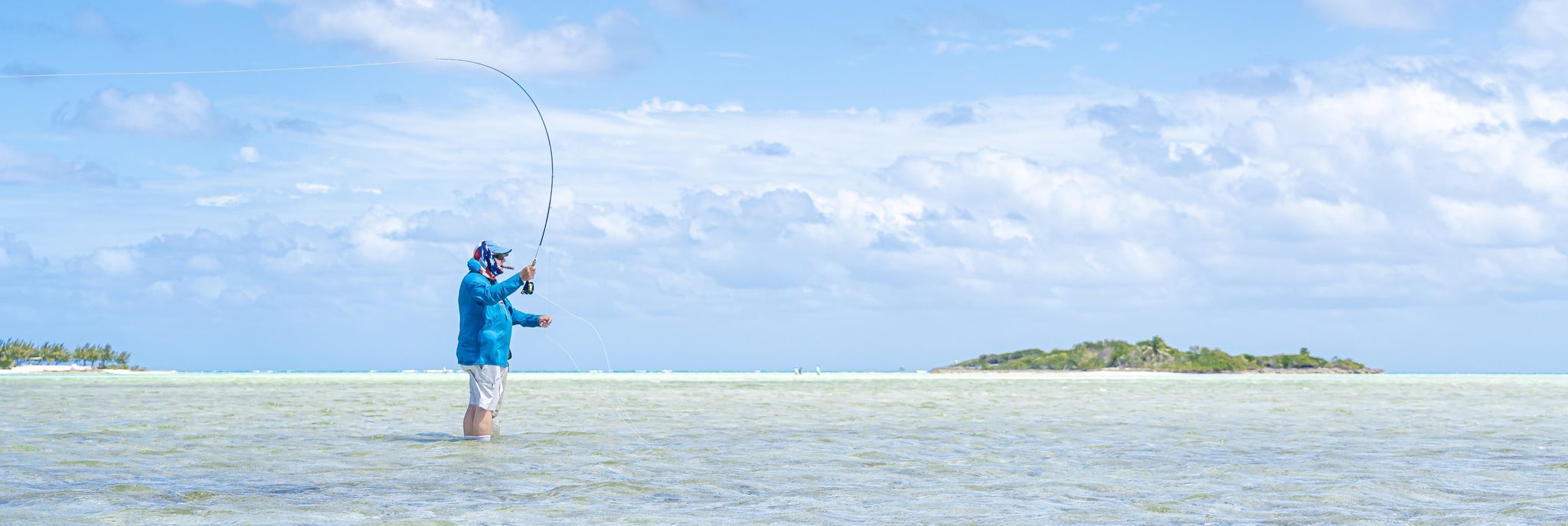 Angler in a blue sunshirt on pale Bahamian flats, fly rod loaded. Photo Adam Campesi, Campesi Design.