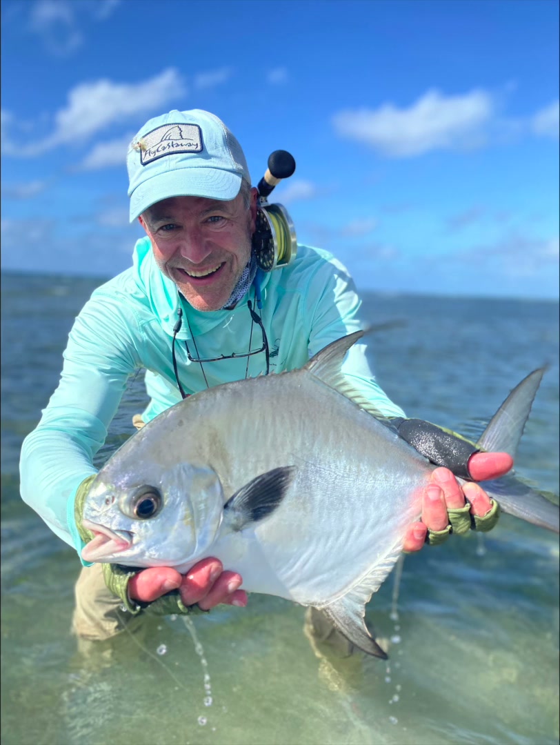 Angler grinning as he holds a permit on the flats at Turneffe Flats, Belize