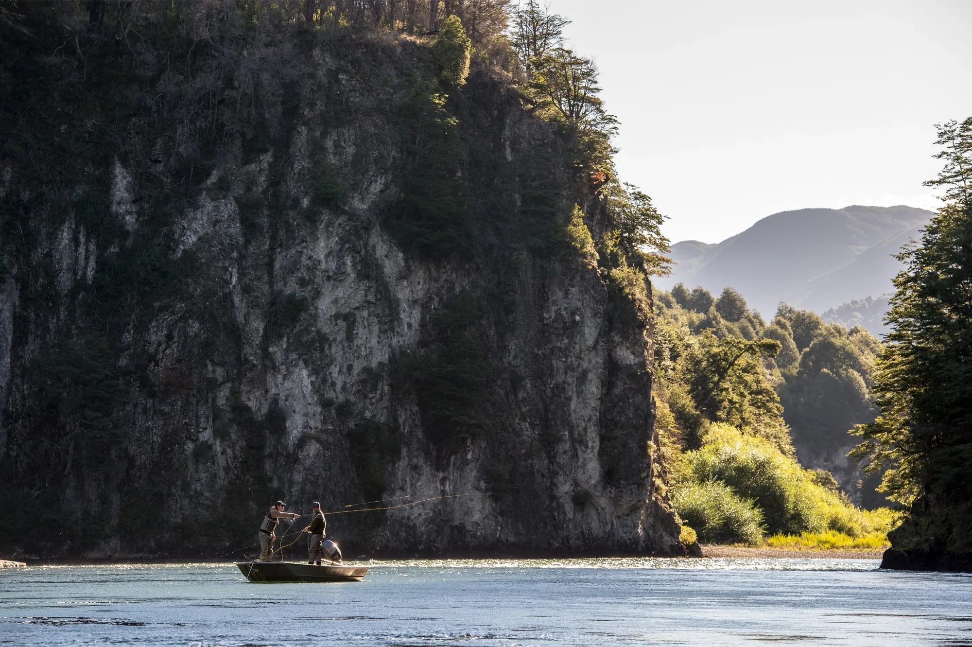Anglers casting from a boat beneath a cliff on a river in northern Chilean Patagonia