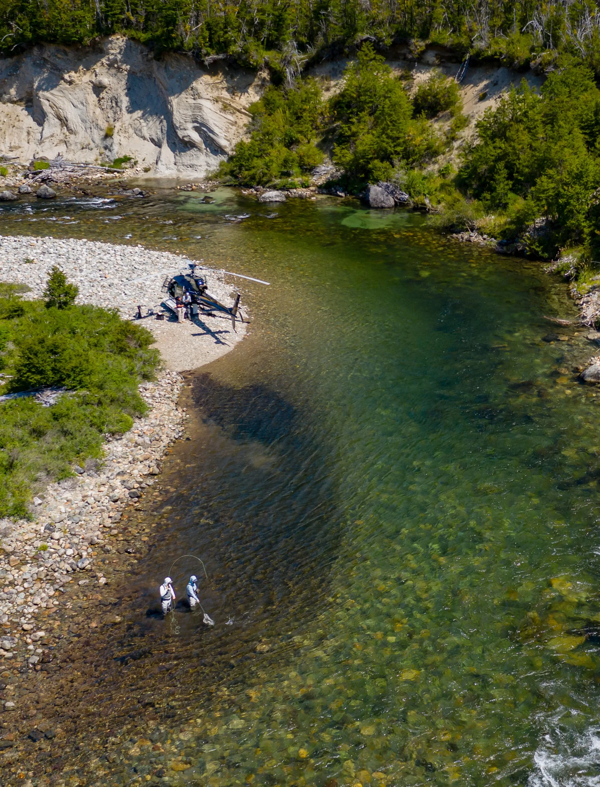Helicopter on a gravel bar while two anglers wade a clear river in northern Chilean Patagonia