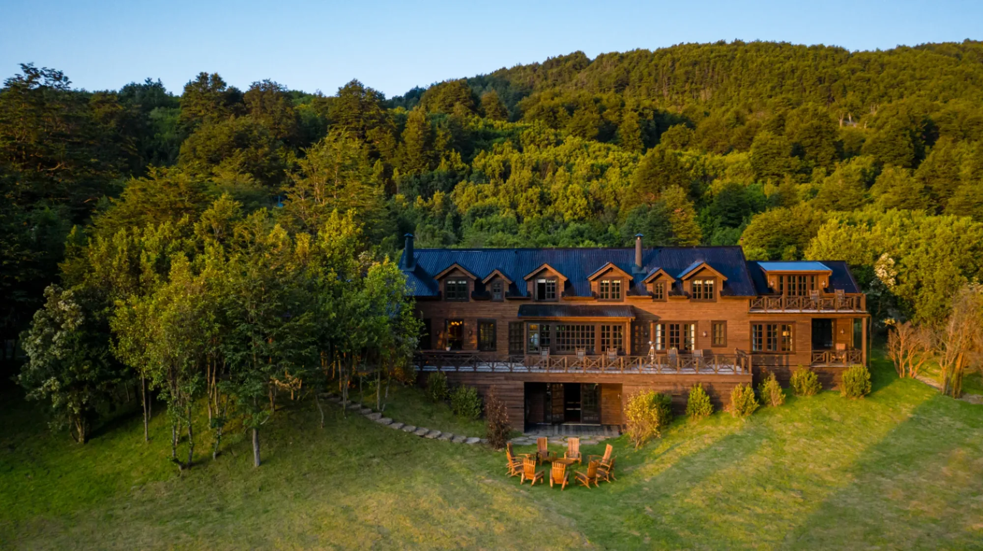 Eleven Rio Palena Lodge, a wooden lodge on a lawn below forested hills in northern Chilean Patagonia