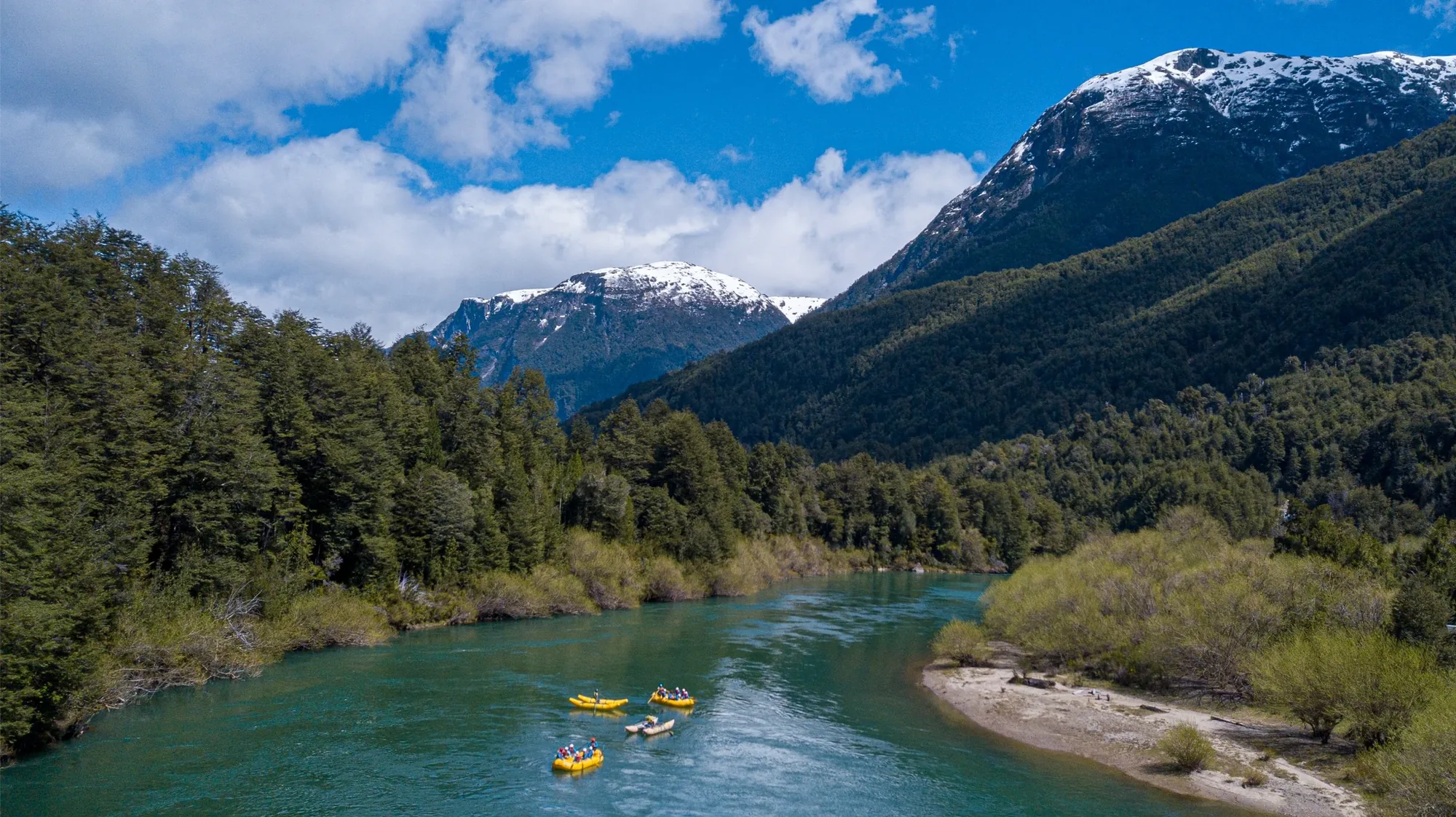 Yellow rafts on a turquoise river below snowy peaks in northern Chilean Patagonia