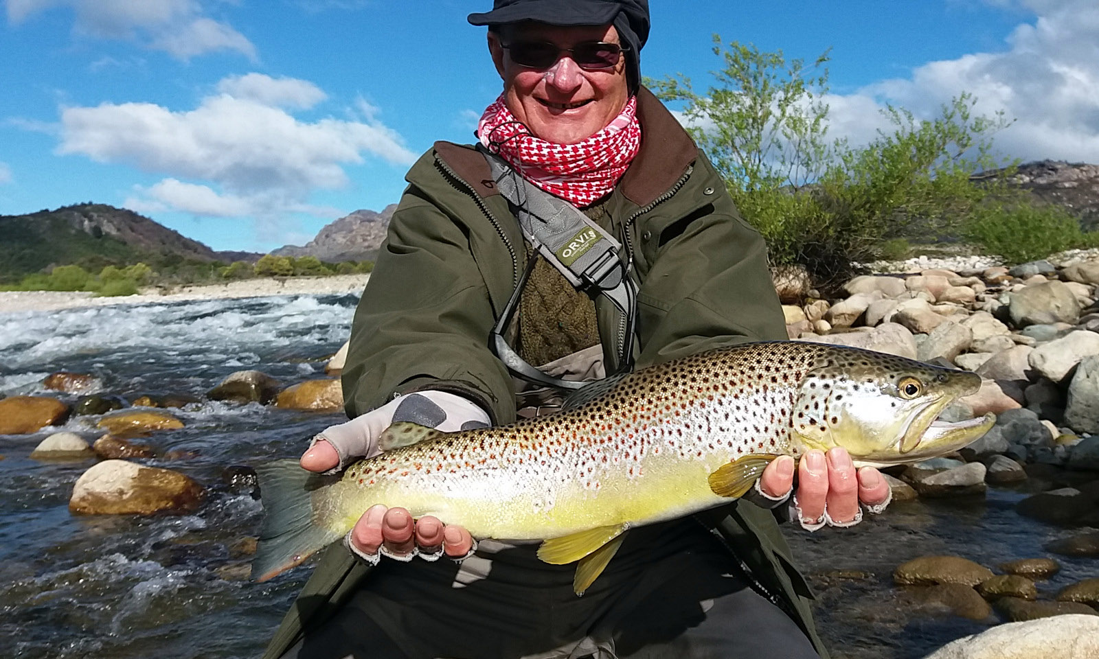 Angler holding a brown trout on a rocky Chilean Patagonia river, Three River Lodge