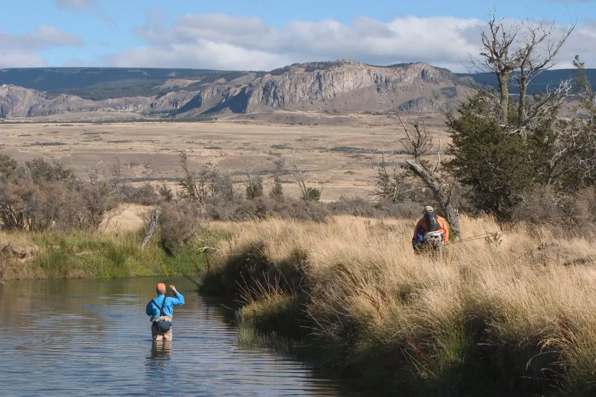Angler wading a spring creek in a wide valley below rock cliffs, El Saltamontes Lodge